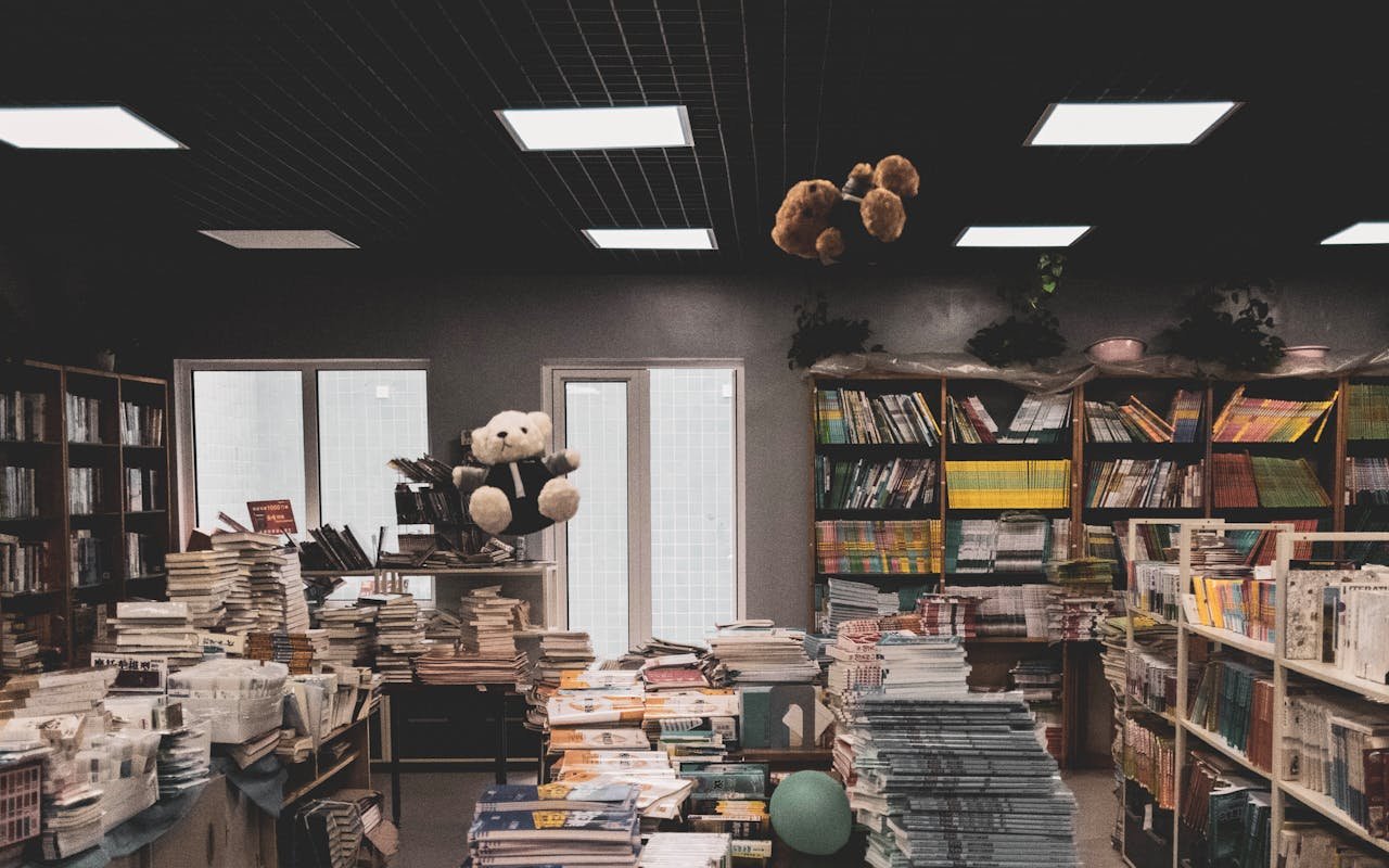 Cozy bookstore interior with stacks of books, teddy bears, and shelves, creating a warm and inviting atmosphere.